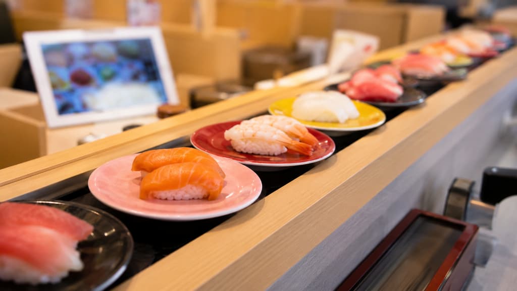 Plates of sushi moving along a conveyor belt at an affordable kaiten-zushi restaurant in Japan