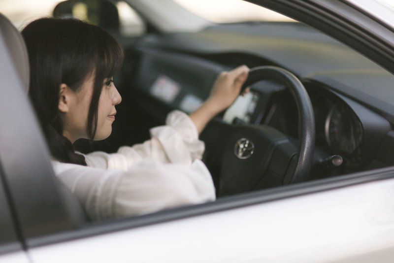 A driver's hands on the wheel of a car on a Japanese road