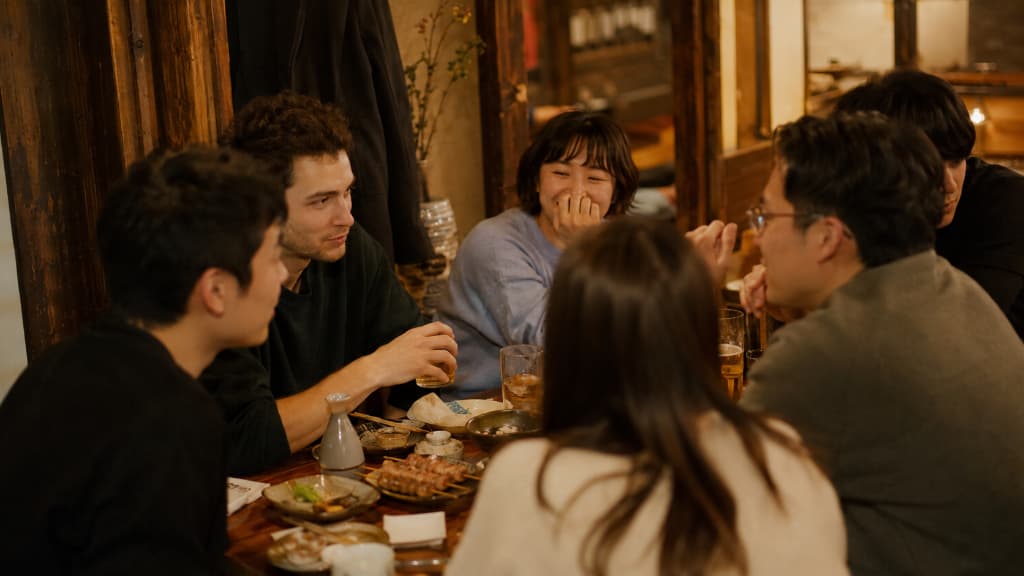 A diverse group of friends laughing together at an izakaya in Japan